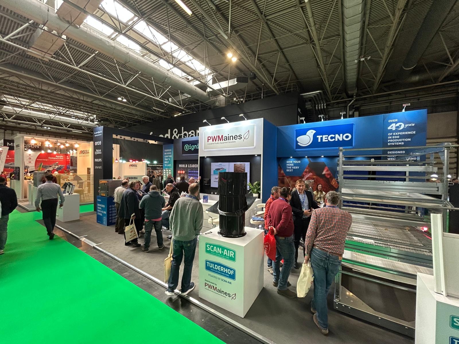 Exhibition stand displaying PW Maines poultry equipment as attendees ask about housing, lighting, and ventilation solutions.
