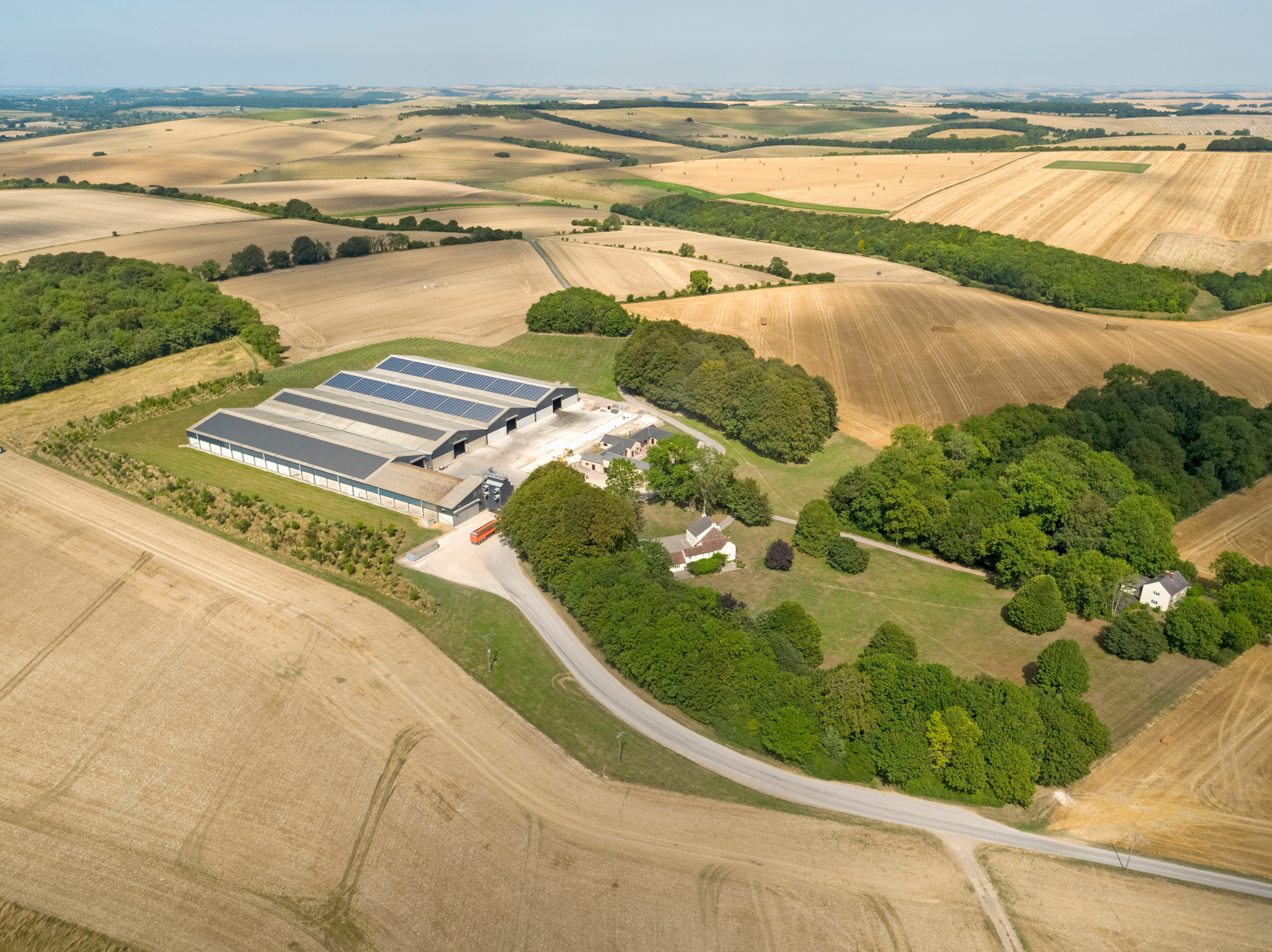 A modern poultry house complex sits among large agricultural fields in the countryside.